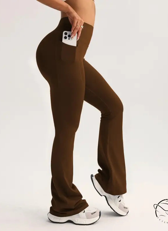 Brown high-waisted flared langry yoga pants with side pocket holding white smartphone