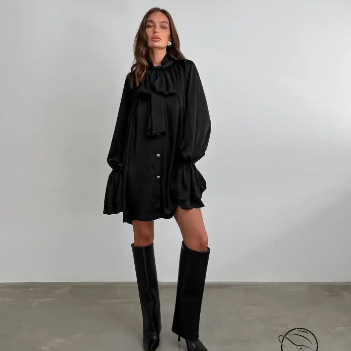 Elegant black satin dress with ruffles, long sleeves, and knee-high boots